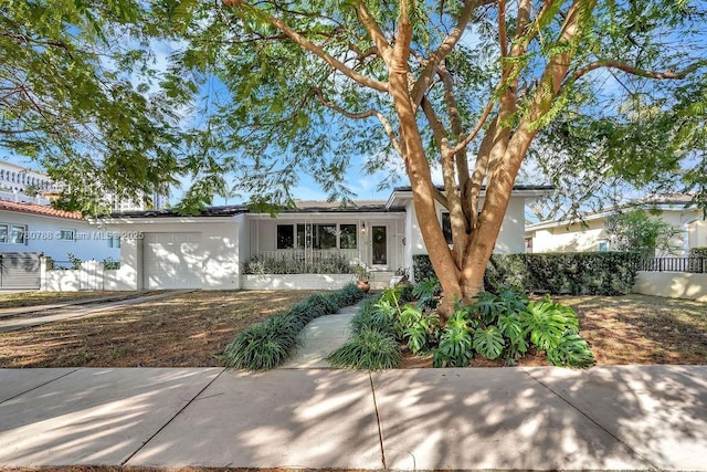 ranch-style home featuring stucco siding, fence, covered porch, and a garage