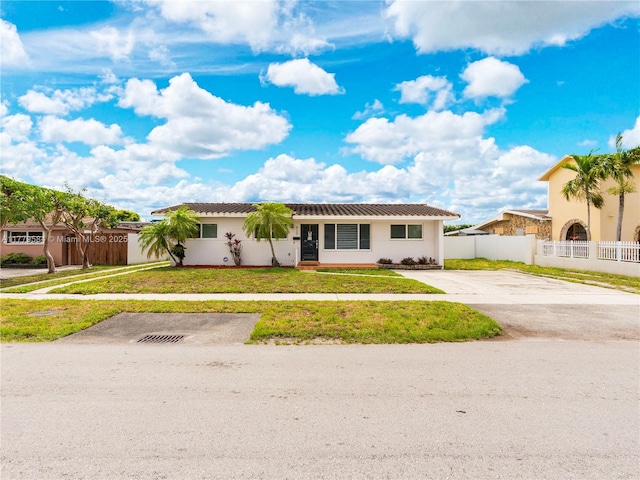 ranch-style house featuring a front lawn, fence, stucco siding, and concrete driveway