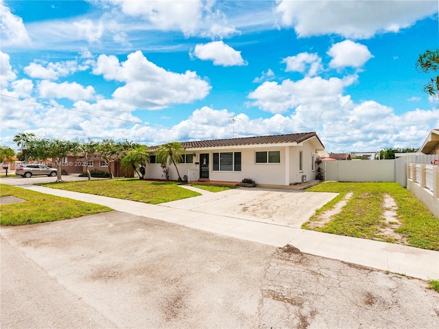 ranch-style home with stucco siding, driveway, a front lawn, a tiled roof, and fence
