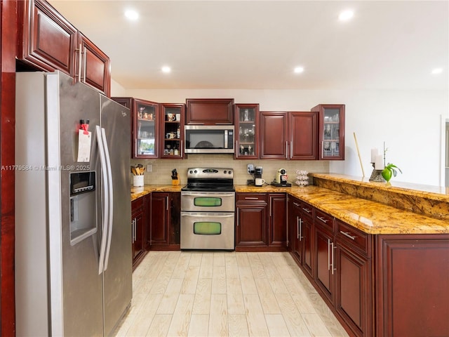 kitchen featuring appliances with stainless steel finishes, a peninsula, dark brown cabinets, light wood finished floors, and decorative backsplash