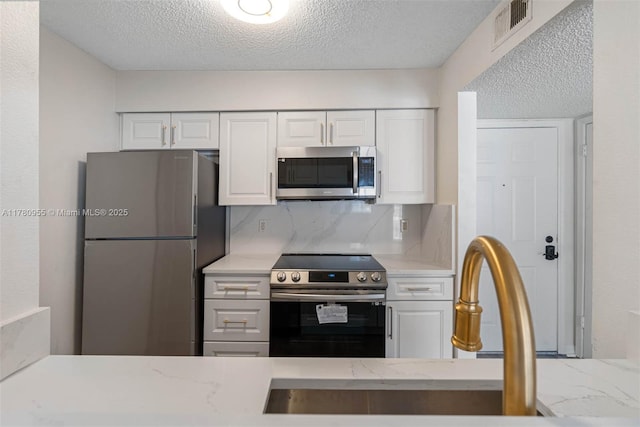 kitchen with tasteful backsplash, visible vents, appliances with stainless steel finishes, and white cabinetry