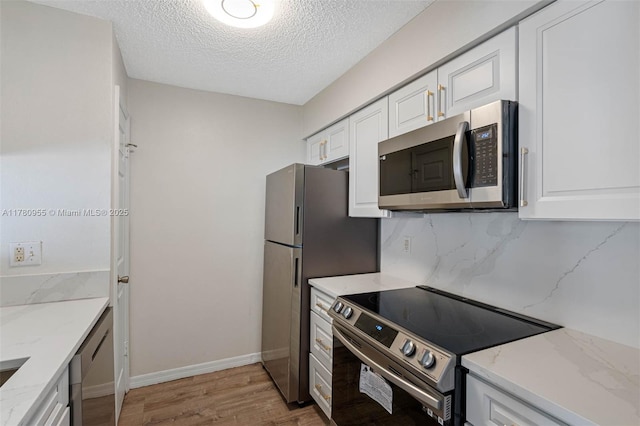 kitchen featuring light wood-style floors, white cabinetry, appliances with stainless steel finishes, light stone counters, and decorative backsplash