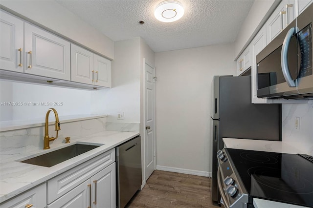 kitchen featuring white cabinetry, light stone countertops, dark wood-type flooring, appliances with stainless steel finishes, and a sink