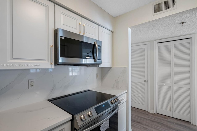 kitchen with tasteful backsplash, white cabinets, visible vents, stainless steel appliances, and wood finished floors