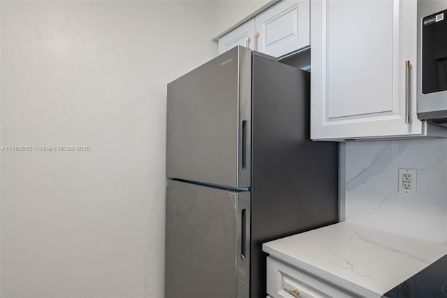 kitchen with tasteful backsplash, white cabinets, light stone counters, and stainless steel appliances