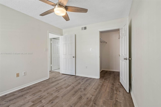 unfurnished bedroom with a walk in closet, a textured ceiling, baseboards, and wood finished floors
