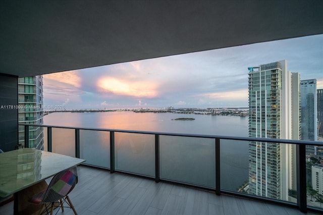 balcony at dusk featuring a water view and outdoor dining space