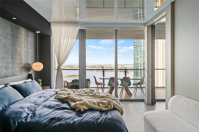 bedroom with light wood-style flooring, floor to ceiling windows, a water view, and access to exterior