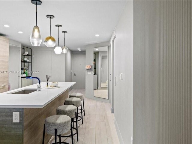 kitchen featuring a breakfast bar, a sink, light countertops, recessed lighting, and light wood-type flooring