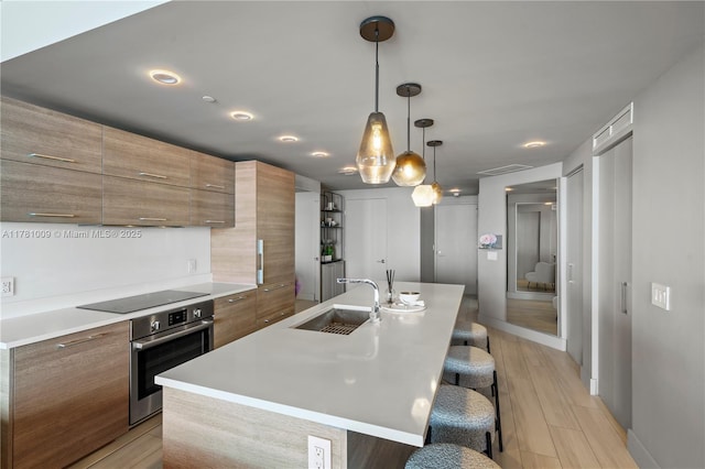 kitchen featuring brown cabinets, a sink, a kitchen breakfast bar, black electric cooktop, and stainless steel oven
