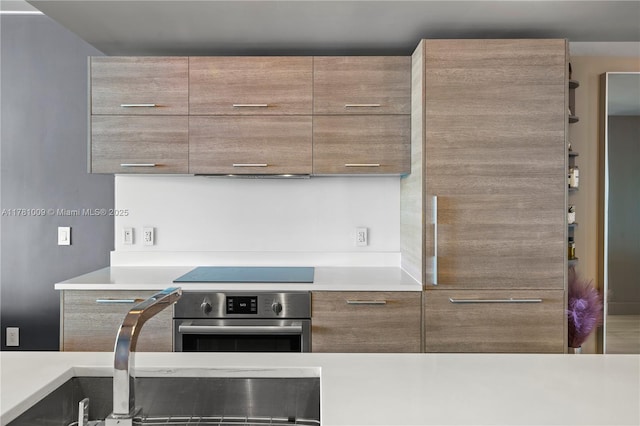 kitchen with oven, black electric stovetop, a sink, light countertops, and modern cabinets
