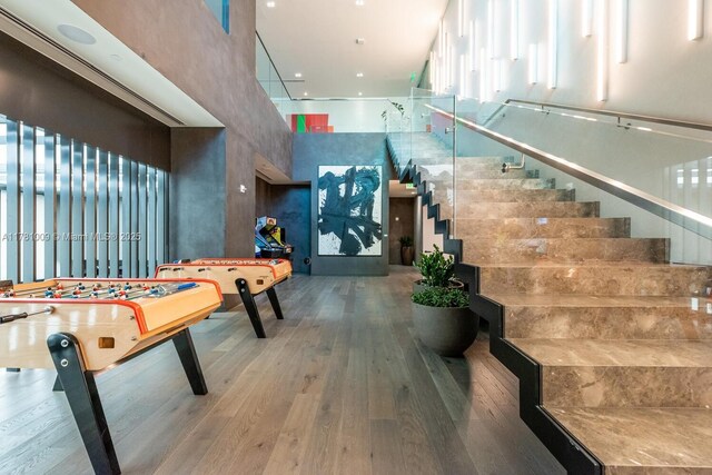 recreation room featuring a high ceiling, a healthy amount of sunlight, and hardwood / wood-style flooring