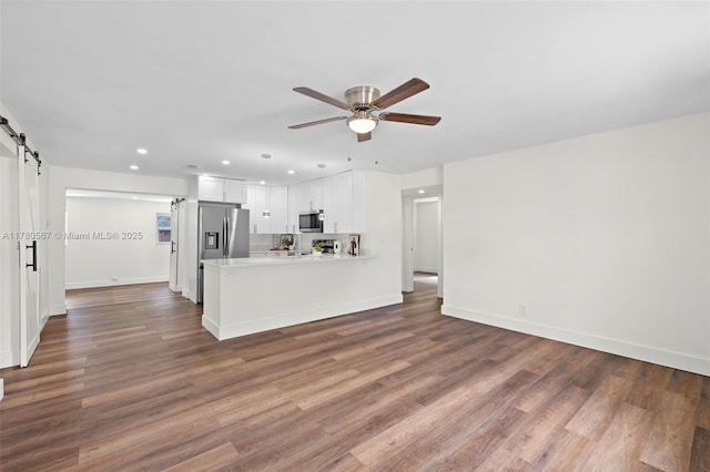 unfurnished living room with a barn door, dark wood-style flooring, baseboards, and ceiling fan
