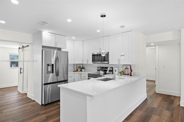 kitchen featuring a peninsula, visible vents, a barn door, appliances with stainless steel finishes, and light countertops