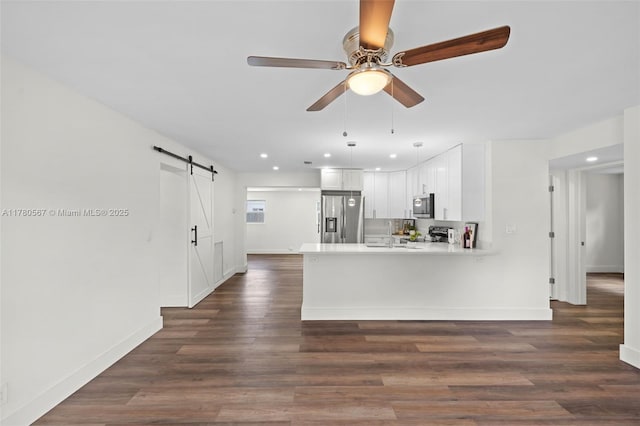 kitchen with a peninsula, white cabinetry, light countertops, a barn door, and stainless steel appliances