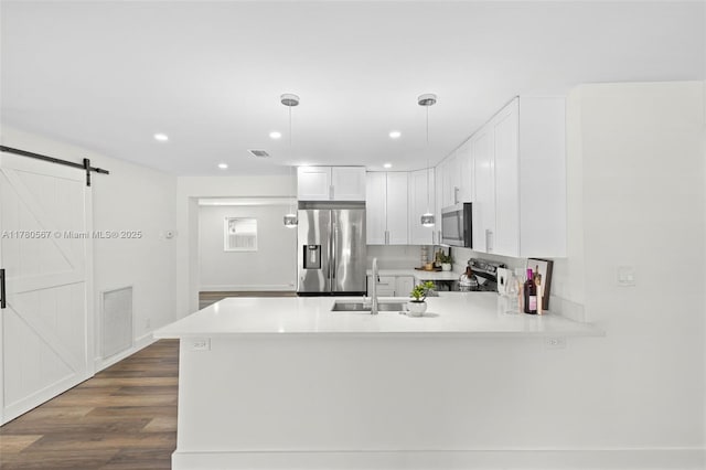 kitchen with a peninsula, visible vents, a barn door, appliances with stainless steel finishes, and a sink