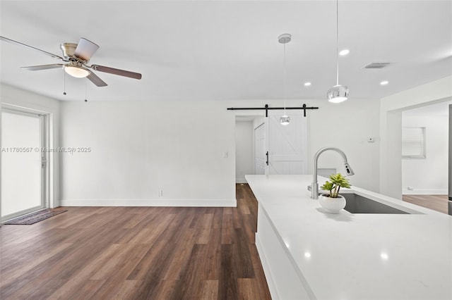 kitchen with a ceiling fan, a barn door, visible vents, dark wood finished floors, and a sink