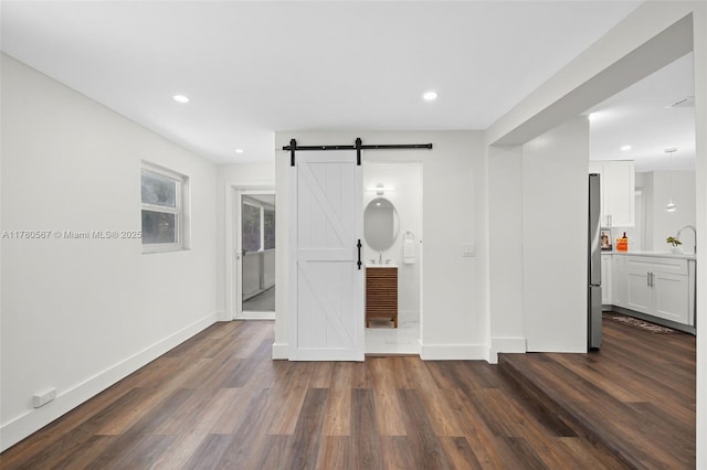 unfurnished bedroom featuring dark wood-type flooring, recessed lighting, a barn door, a sink, and baseboards