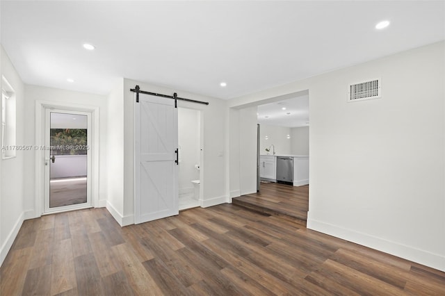 empty room with baseboards, recessed lighting, dark wood-style floors, a barn door, and visible vents