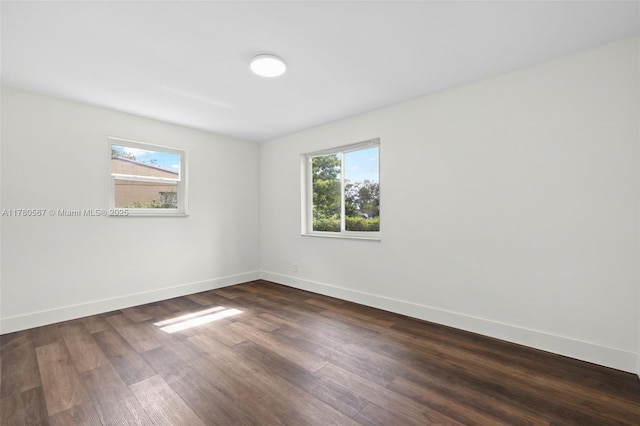 empty room featuring a healthy amount of sunlight, baseboards, and dark wood finished floors
