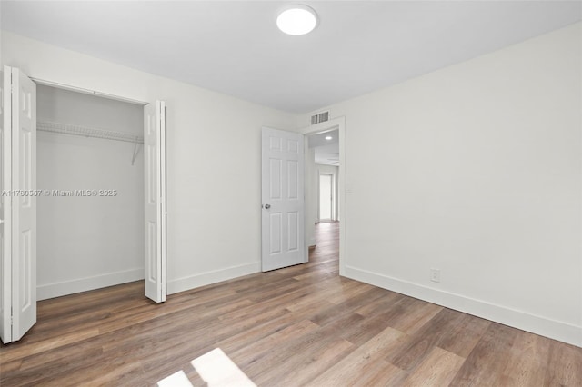 unfurnished bedroom featuring a closet, visible vents, baseboards, and wood finished floors