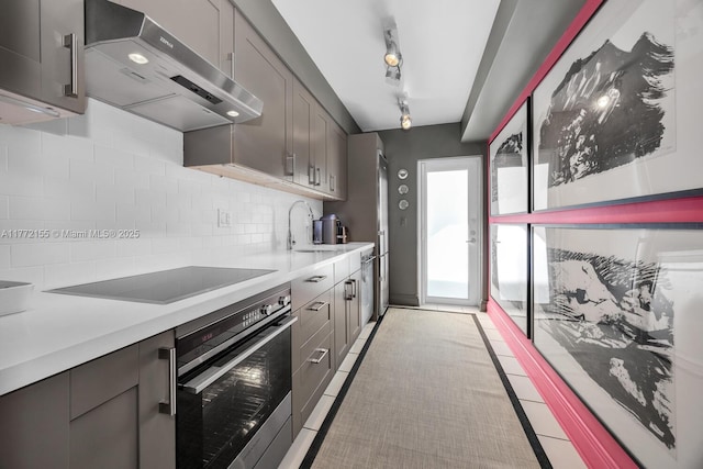 kitchen with a sink, oven, black electric cooktop, light countertops, and range hood