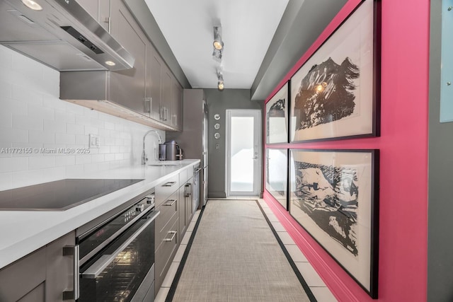 kitchen featuring a sink, stainless steel oven, decorative backsplash, black electric stovetop, and under cabinet range hood