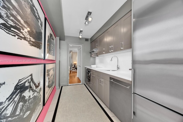 kitchen featuring a sink, gray cabinetry, light countertops, under cabinet range hood, and appliances with stainless steel finishes