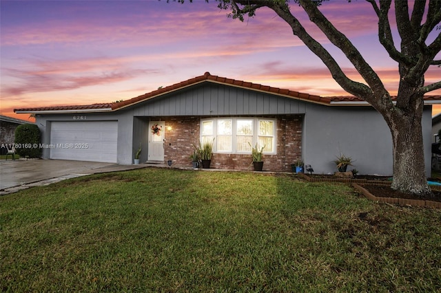 ranch-style home with a tiled roof, a yard, brick siding, a garage, and concrete driveway