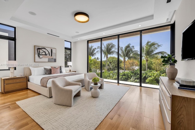 bedroom featuring a wall of windows, light wood-style floors, and a tray ceiling