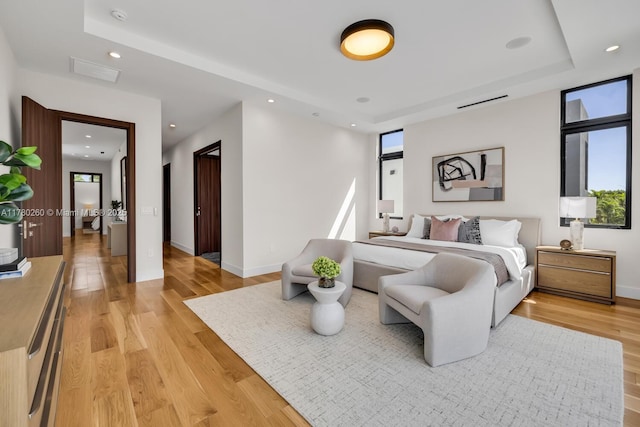 bedroom with multiple windows, a tray ceiling, recessed lighting, and light wood-style flooring