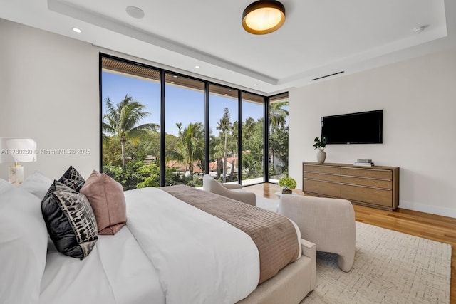 bedroom with recessed lighting, a wall of windows, wood finished floors, and a raised ceiling