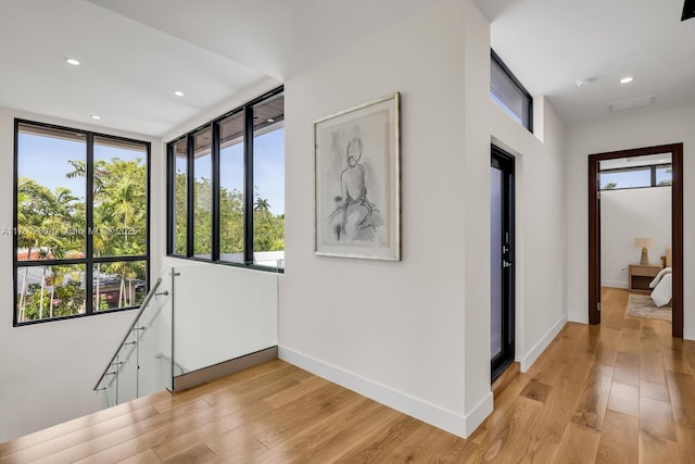 hall featuring baseboards, plenty of natural light, and light wood-style floors