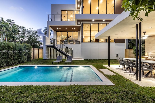 back of property featuring a lawn, fence, stairs, and a balcony