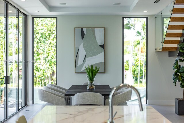 dining space with baseboards, a wall of windows, a tray ceiling, and stairway