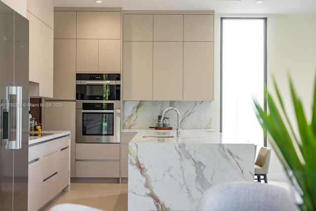 kitchen with light stone counters, stainless steel double oven, a sink, backsplash, and modern cabinets