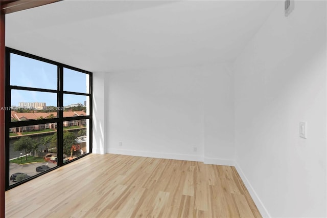 unfurnished room with wood finished floors, baseboards, and a wall of windows