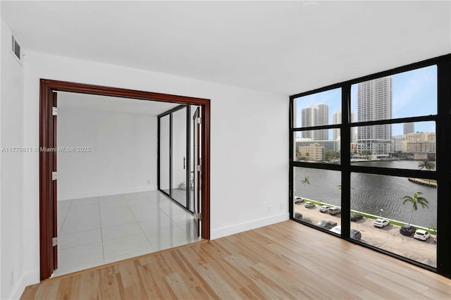 empty room featuring floor to ceiling windows, visible vents, wood finished floors, a view of city, and baseboards