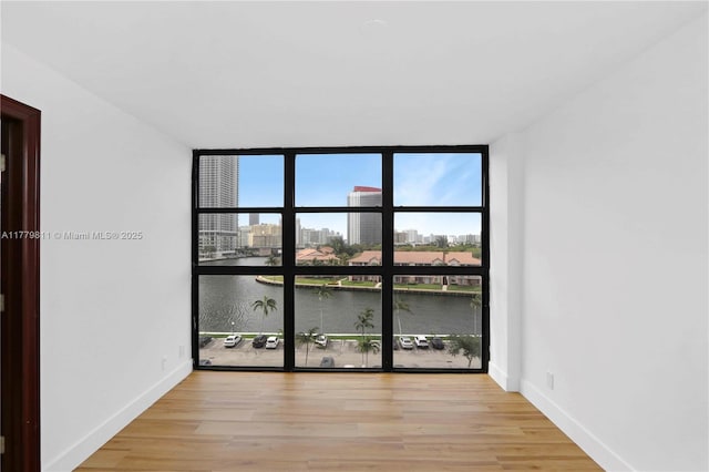 spare room with light wood finished floors, baseboards, a wall of windows, and a water view