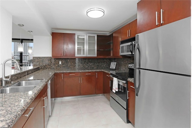 kitchen with dark stone countertops, glass insert cabinets, backsplash, stainless steel appliances, and a sink