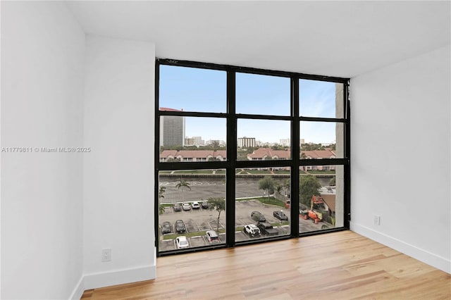 unfurnished room with a wall of windows, a wealth of natural light, wood finished floors, and baseboards