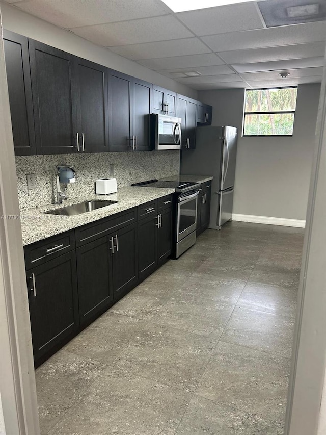 kitchen with appliances with stainless steel finishes, a sink, dark cabinetry, baseboards, and backsplash