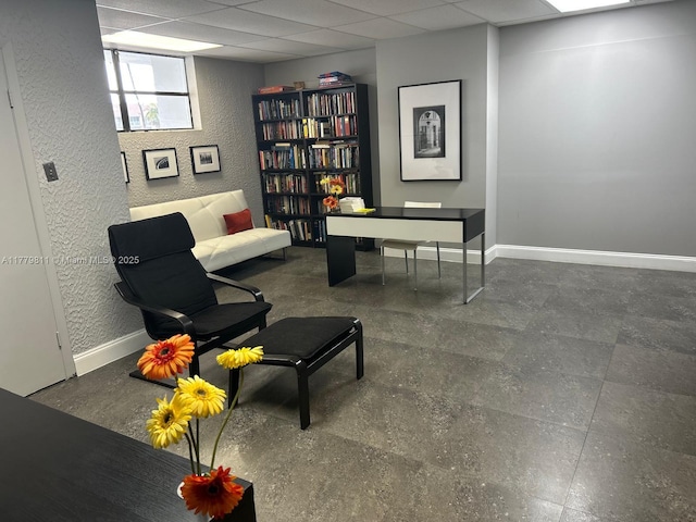 sitting room with a textured wall, baseboards, and a drop ceiling