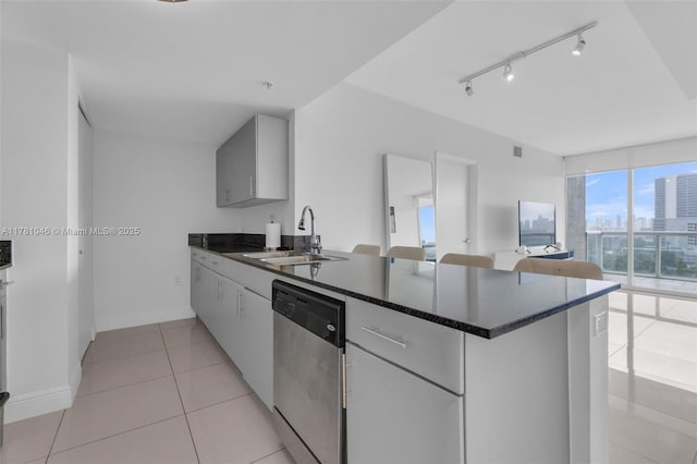kitchen with a peninsula, stainless steel dishwasher, a sink, baseboards, and light tile patterned floors