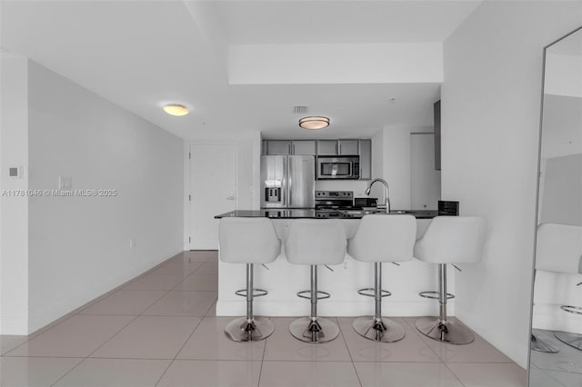 kitchen with dark countertops, stainless steel appliances, baseboards, a kitchen bar, and a peninsula