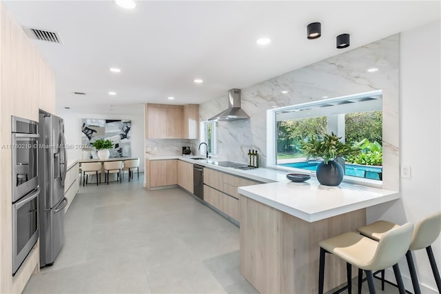 7551 SW 109th Ter, Pinecrest, FL 33156 - kitchen featuring modern cabinets, light brown cabinetry, wall chimney range hood, appliances with stainless steel finishes, and a peninsula