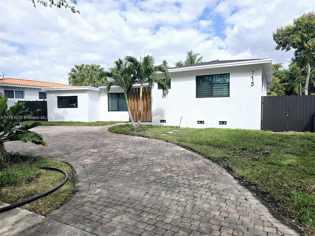 view of front of house featuring a front lawn, decorative driveway, stucco siding, and fence