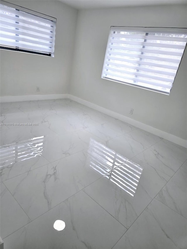 spare room featuring a healthy amount of sunlight, marble finish floor, and baseboards