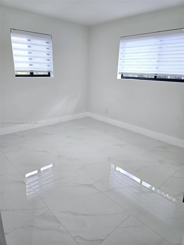 unfurnished room with baseboards, a healthy amount of sunlight, and marble finish floor