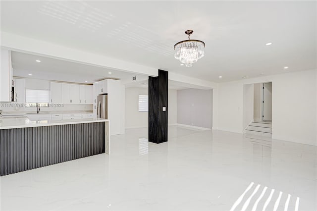 unfurnished living room featuring recessed lighting, an inviting chandelier, marble finish floor, and a sink